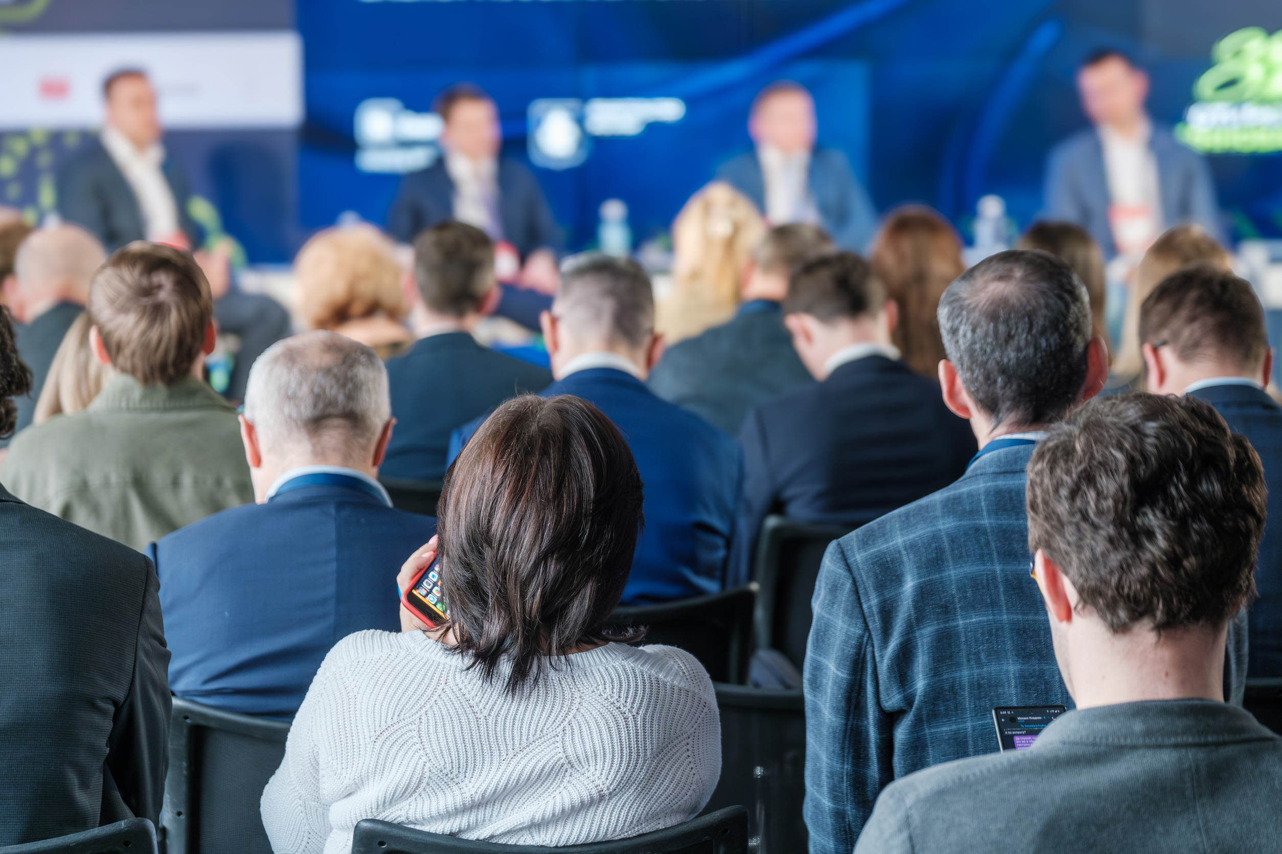 A group of people attentively listening during a business conference or seminar. The event features professional speakers and engaged attendees.